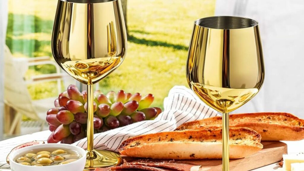 two gold wine glasses on the table with grapes and food
