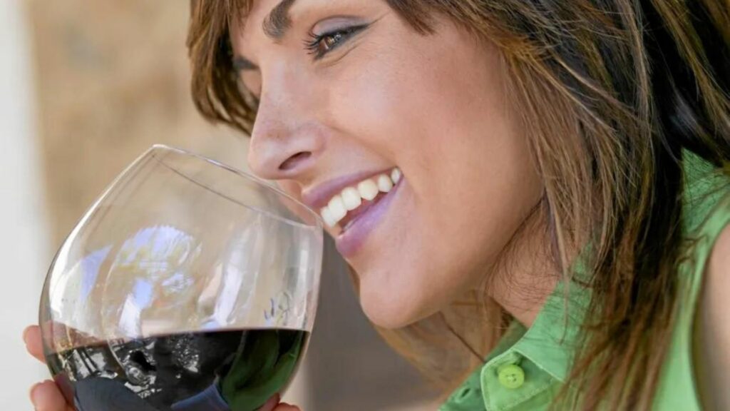 A lady smiling while holding a glass of wine tasting wine